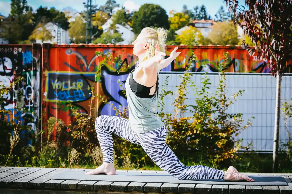 Yoga in der Natur vor Graffiti-Mauer, Yoga Yoga Sonnenberg, entspannter Yoga-Übung im Freien. Frau in Yoga-Pose auf Anti-Rutsch-Matte, kreative sportliche Aktivitäten beim Yoga, Fitness und Wellness im Grünen.